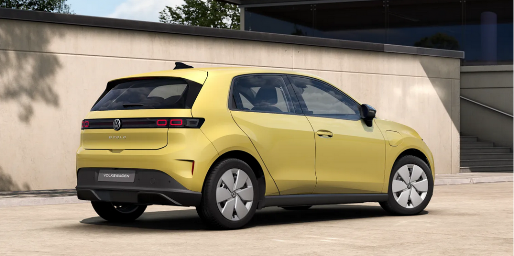 Rear three-quarter view of a yellow Volkswagen ID.3 electric hatchback parked on a light-paved area by a modern building, showing its rear and side profile and VW badge.