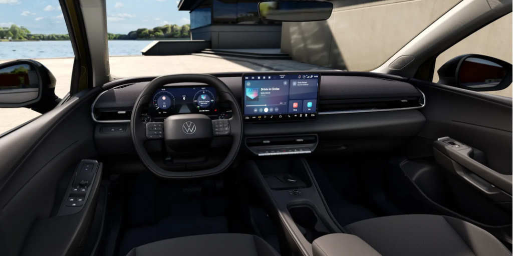 Interior of a modern car cockpit featuring a digital instrument cluster, steering wheel with VW logo, and a large central touchscreen display on the dash overlooking a waterfront scene outside the window.