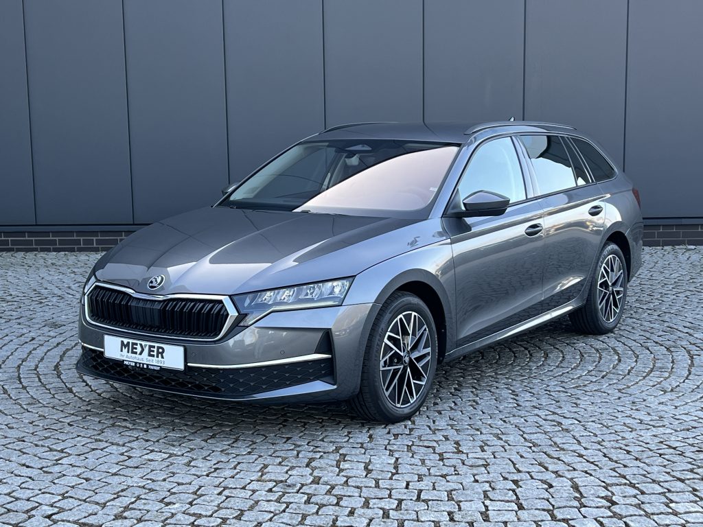 Front three-quarter view of a gray SUV parked on a cobblestone surface against a dark panel wall.