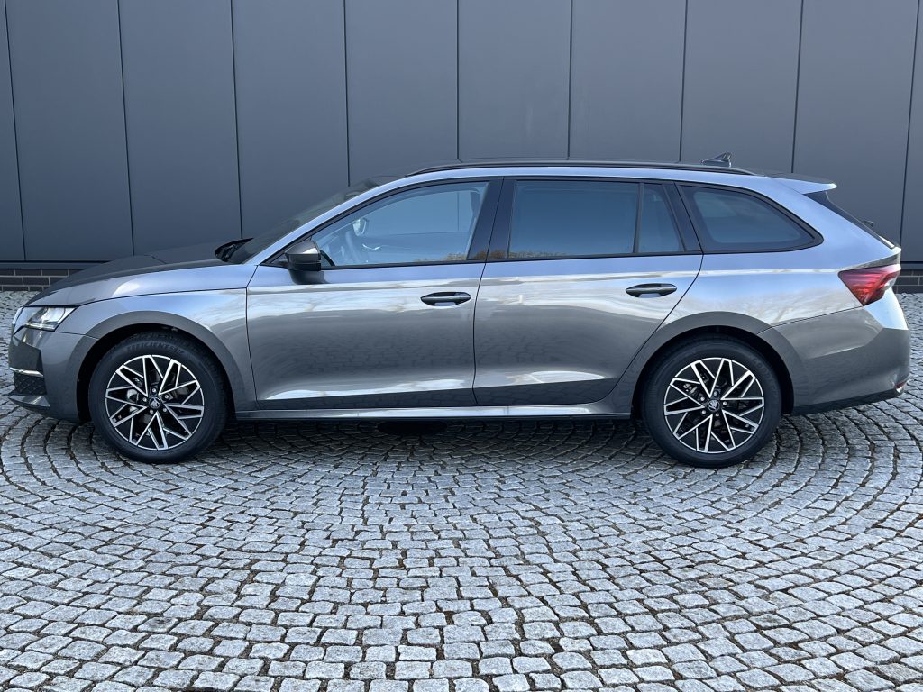Side view of a silver SUV parked on a cobblestone surface in front of a dark grey panel wall