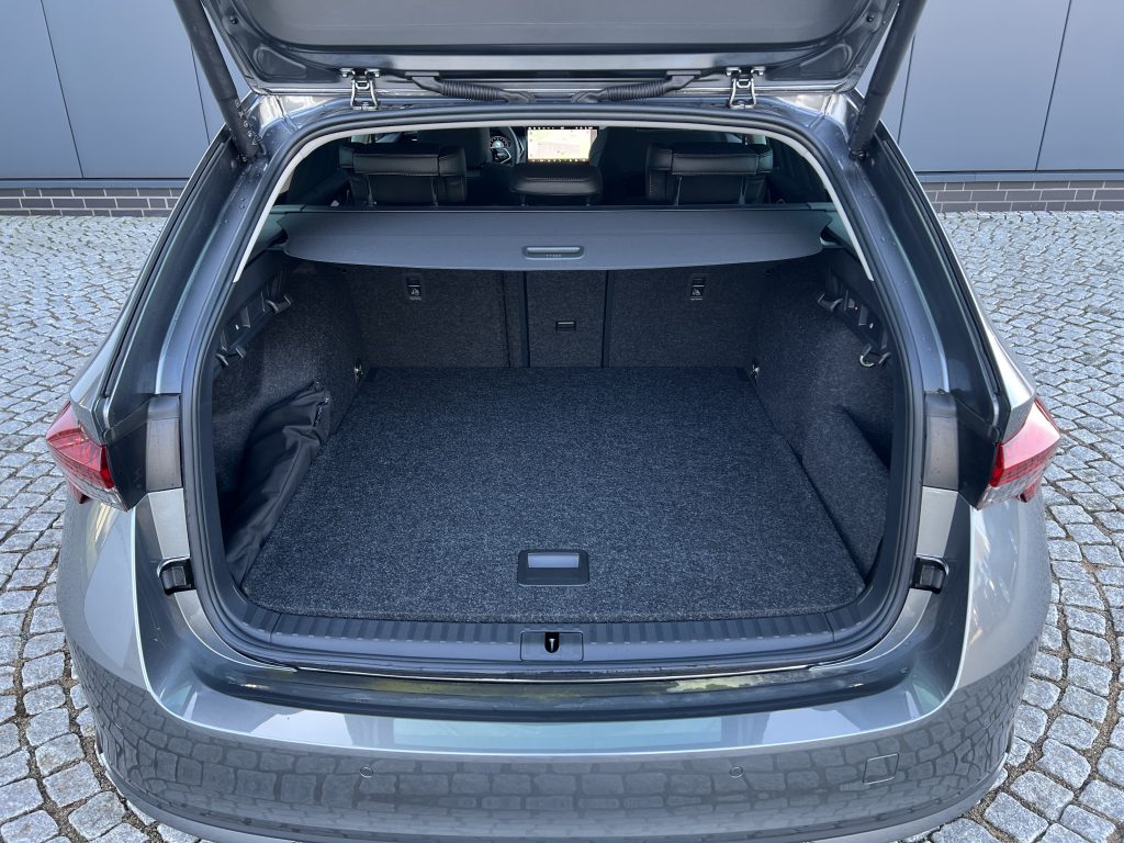 Open hatch of a dark SUV revealing a spacious cargo area with fabric carpeting and folded rear seats visible inside. A dashboard screen is seen through the cabin.