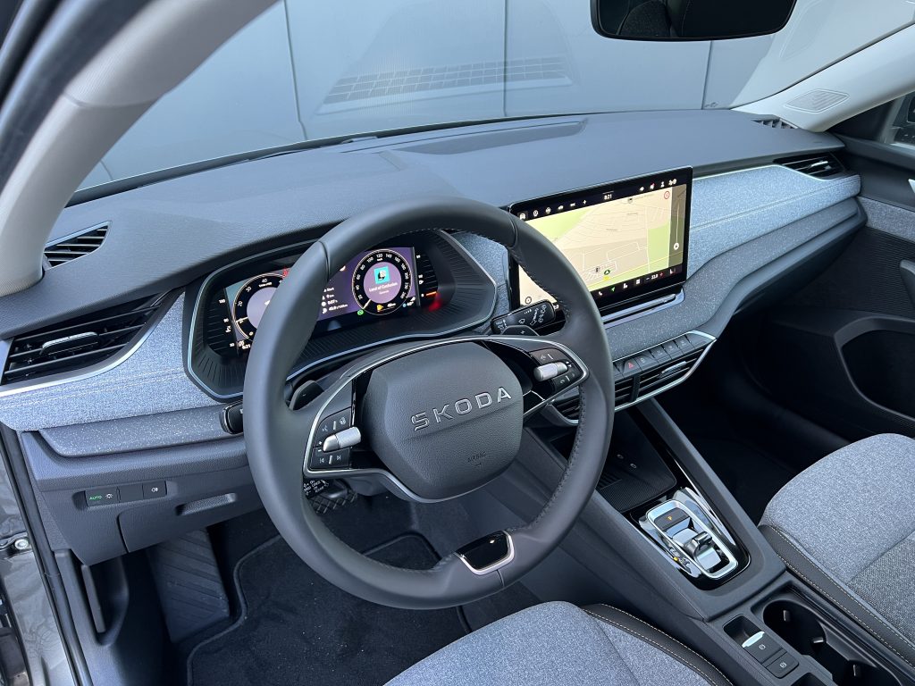 Modern car cockpit with a wide landscape touchscreen showing a navigation map and digital instrument cluster behind the steering wheel