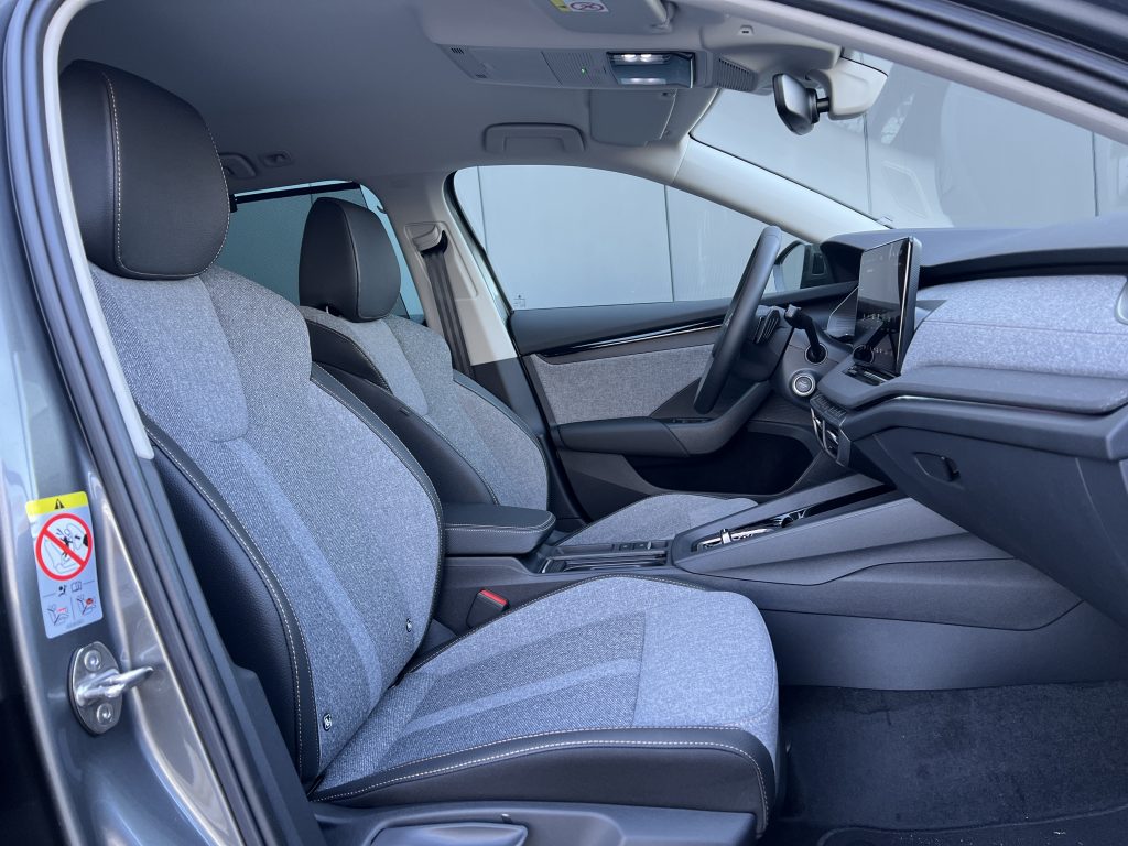 Interior of a right-hand-drive car: front seats, gray fabric upholstery, and a dashboard with a large touchscreen infotainment screen near the steering wheel