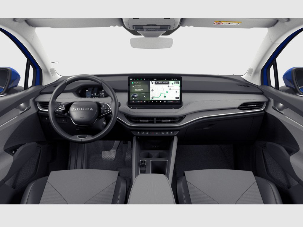 Interior view of a car dashboard from the back seats, with a steering wheel marked Skoda and a large central touchscreen display showing navigation.