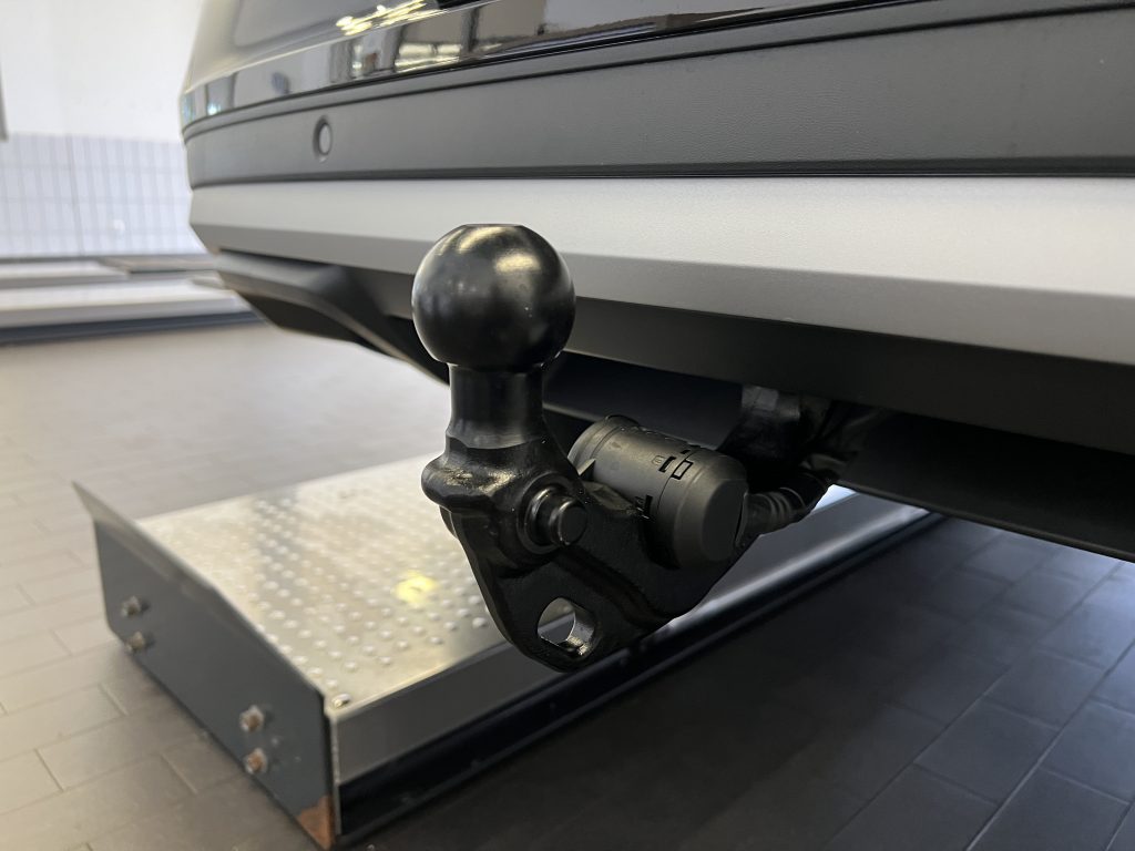 Close-up of a black tow hitch ball mounted to a receiver on a vehicle bumper, indoors in a showroom or workshop setting.