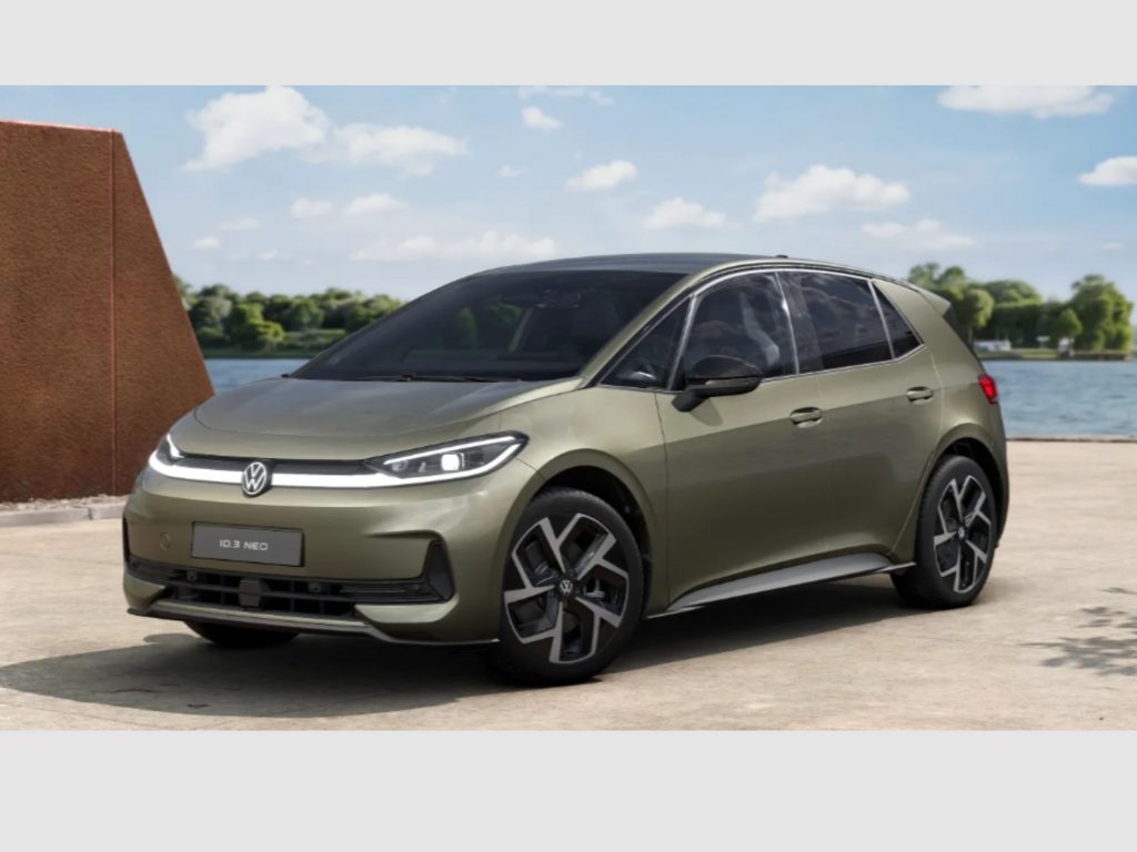 Front three-quarter view of a metallic olive-green VW ID.3 Neo parked beside a lake with a brick structure in the foreground and blue sky overhead, plate reads ID.3 NEO
