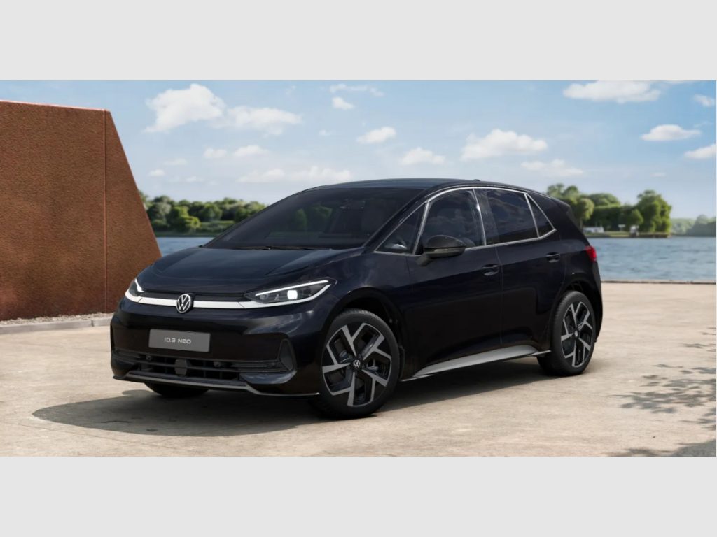 Black Volkswagen ID.3 Neo parked outdoors near a lake with a brown stone wall on the left.