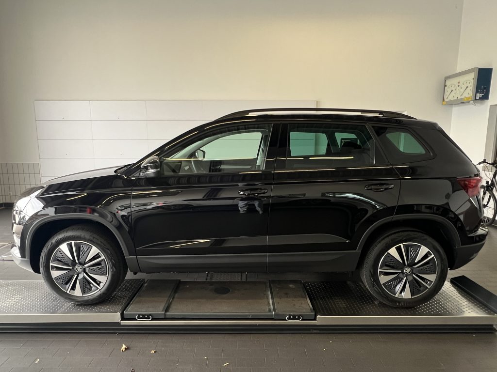 Black SUV on a car lift inside a showroom, viewed from the side with white walls in the background and a bicycle nearby