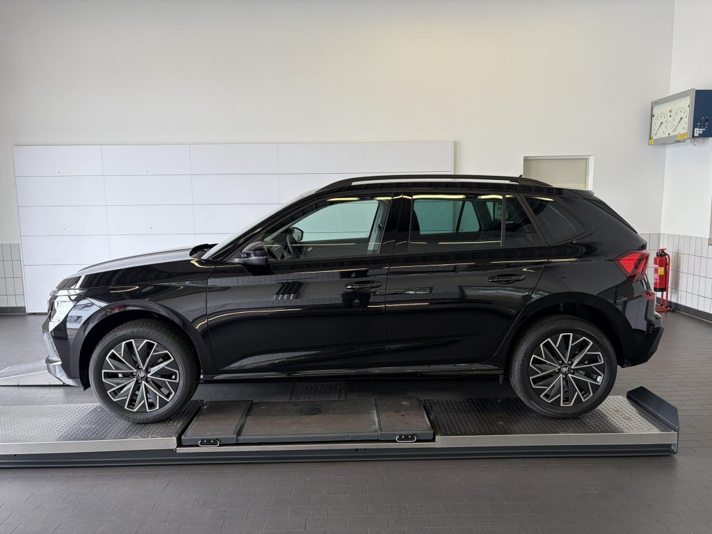 Black SUV on a metal dyno/rolling platform inside a showroom or service bay, with white tiled walls and a fire extinguisher nearby.