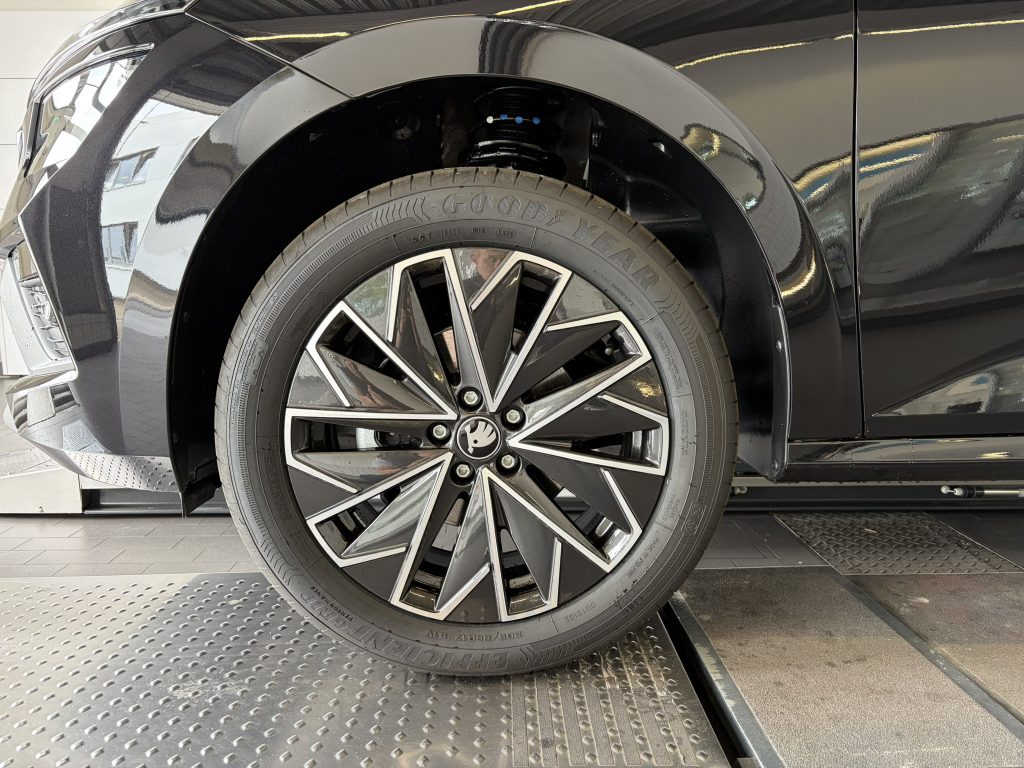 Close-up of a car wheel and tire inside a showroom, showing a glossy black fender and alloy rim with a Goodyear tire.