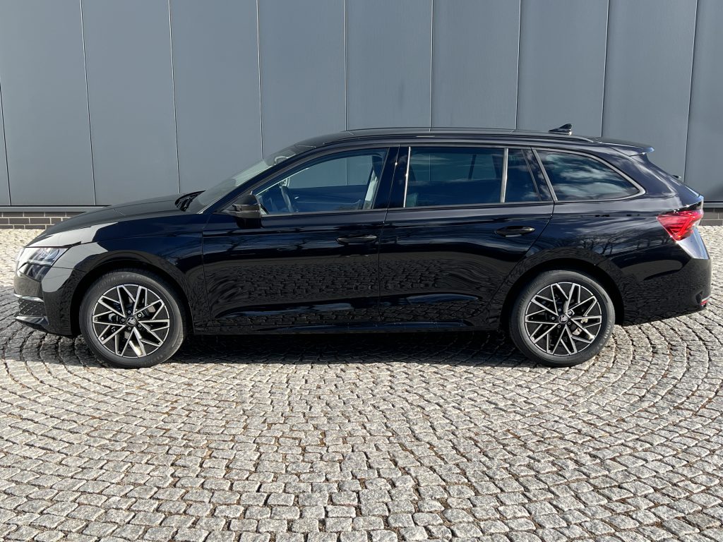 Black SUV parked on a cobblestone surface beside a gray wall, shown in side profile with roof rails and alloy wheels.