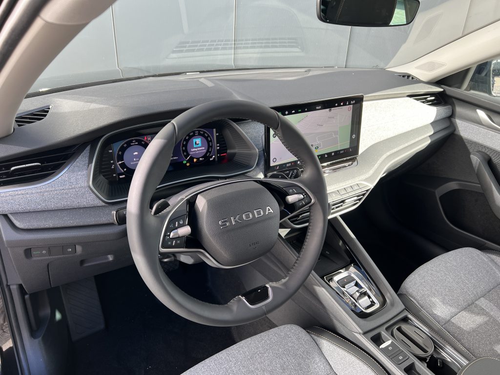 Interior of a car cabin with a digital driver display, a large central touchscreen, and a leather steering wheel.