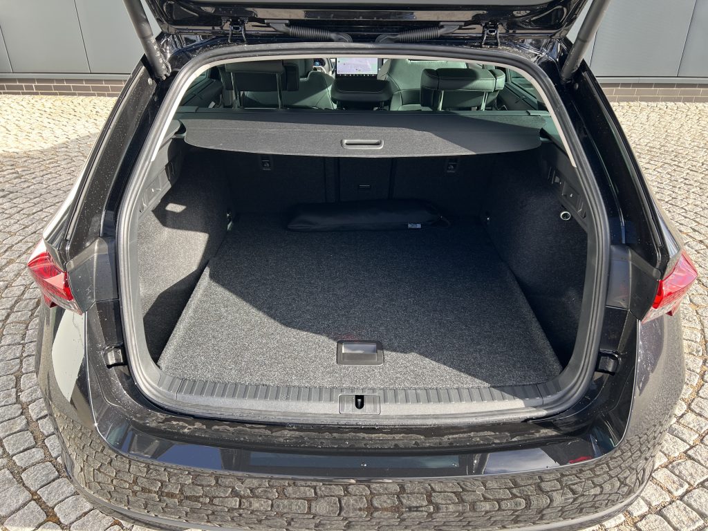 Open car trunk with cargo cover in place, showing empty loading area and rear seats folded forward in a hatchback.