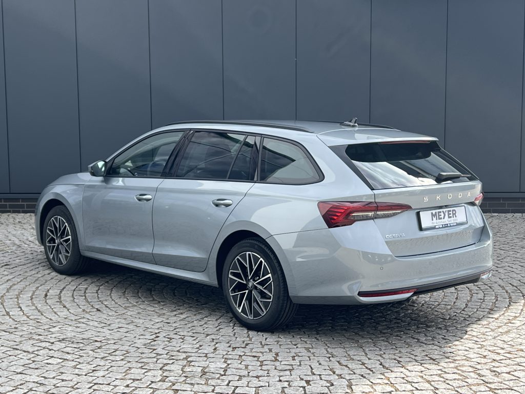 Rear three-quarter view of a silver Skoda Octavia wagon parked on a cobblestone surface against a dark wall.