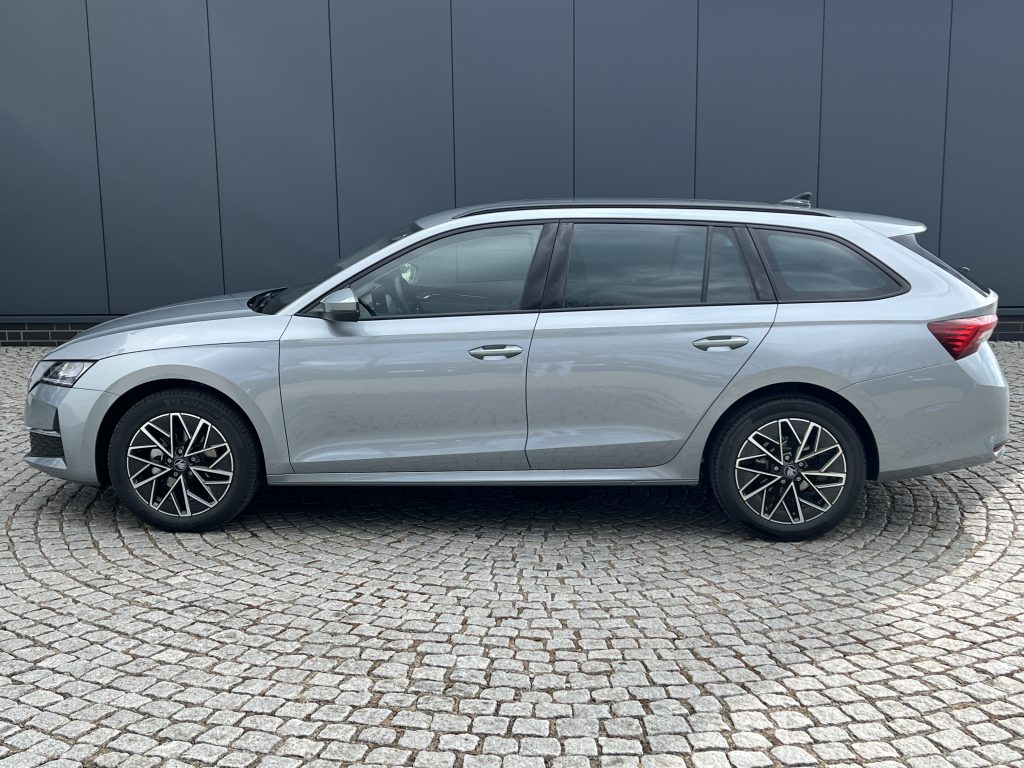 Side profile of a silver SUV with roof rails parked on a cobblestone surface against a dark blue wall.