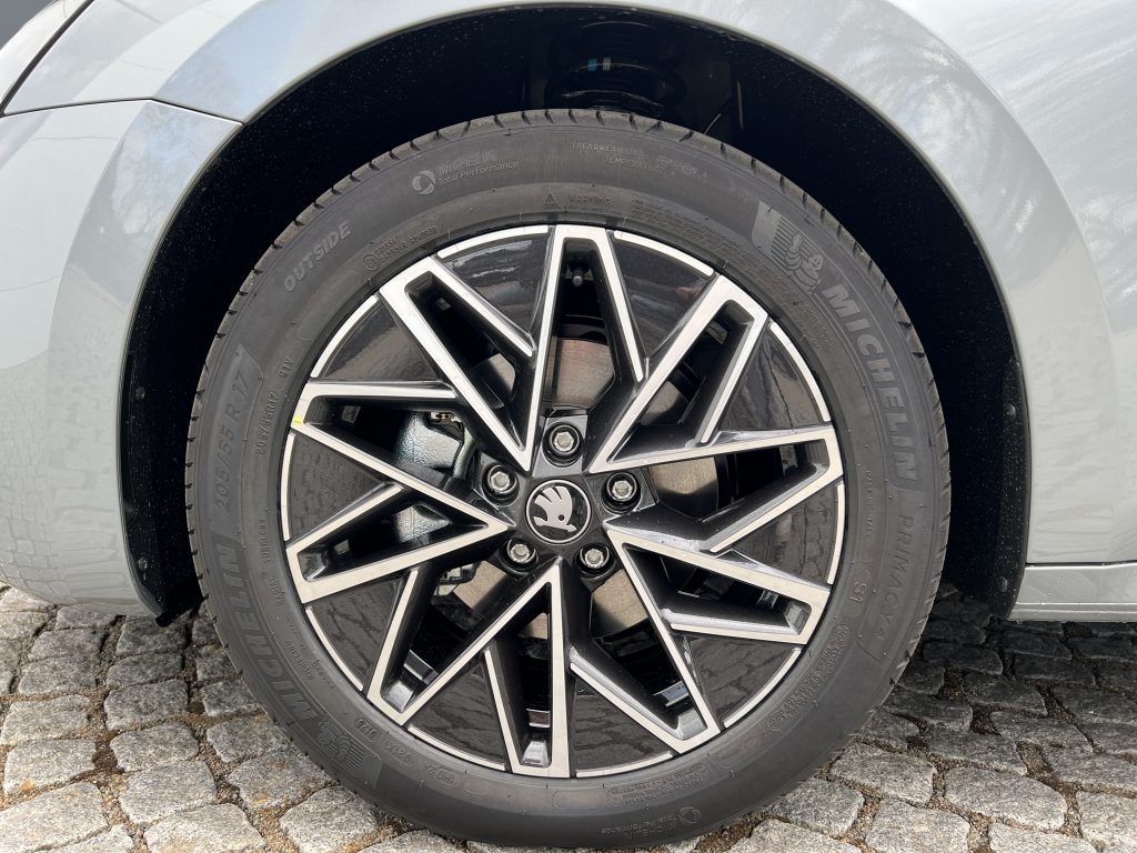Close-up of a silver car wheel with a black and silver alloy rim and a Michelin tire on a cobblestone surface, showing the fender above the wheel.