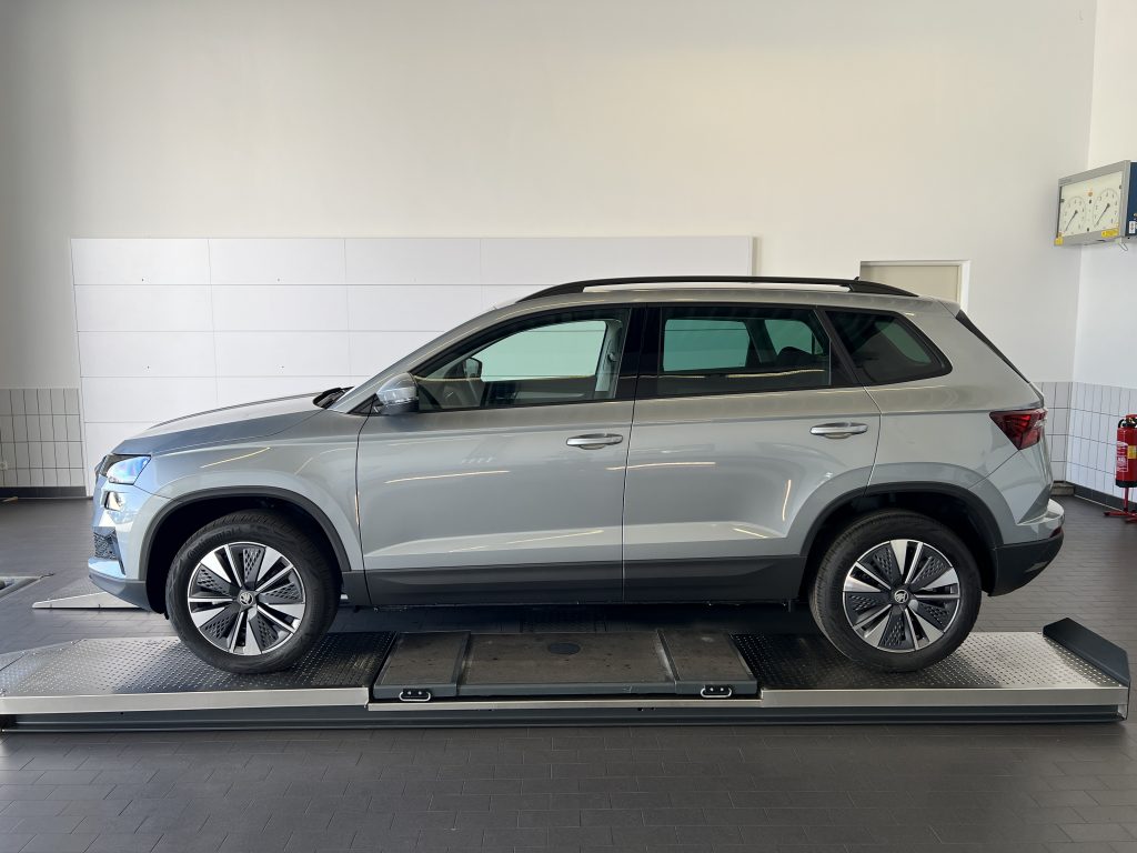 Silver SUV on a car lift in a showroom with white tiled walls.