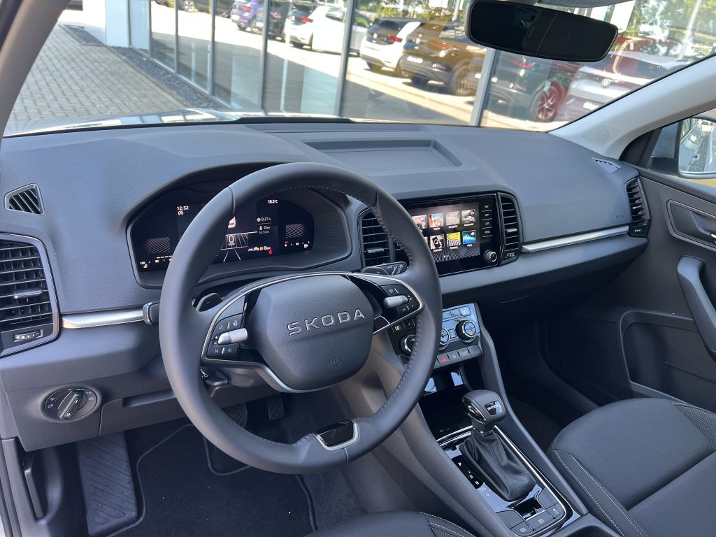 Interior of a modern car cabin showing a steering wheel with SKODA logo, digital instrument cluster, and a touchscreen infotainment system.