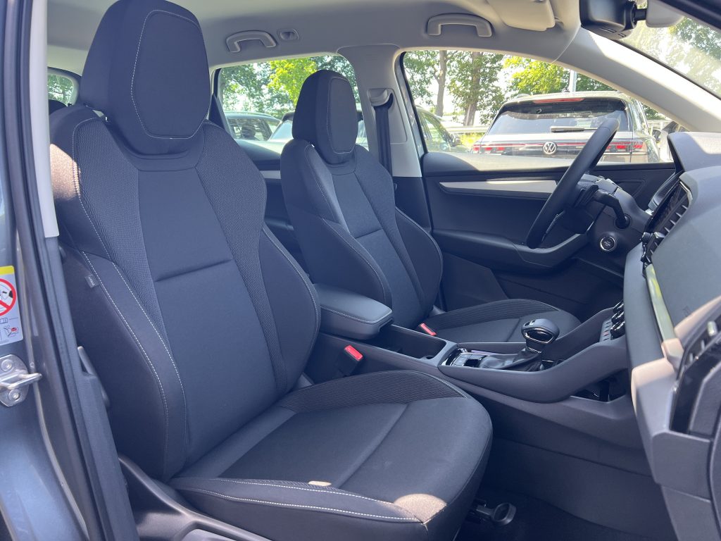Front interior of a car with black fabric seats, steering wheel, and center console; parking lot visible through the windows.