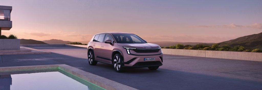 Front three-quarter view of a pink SUV on a modern terrace at sunset, with distant hills in the background.