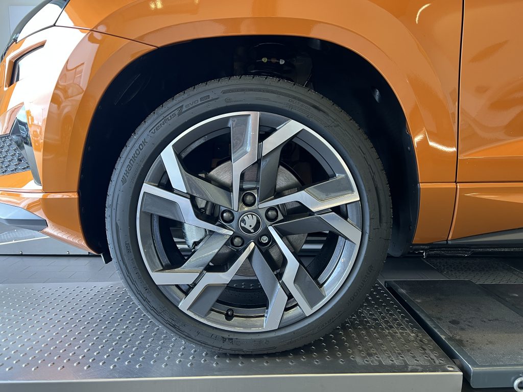 Close-up of an orange car wheel and tire, showing a large alloy rim and brake area behind the fender.