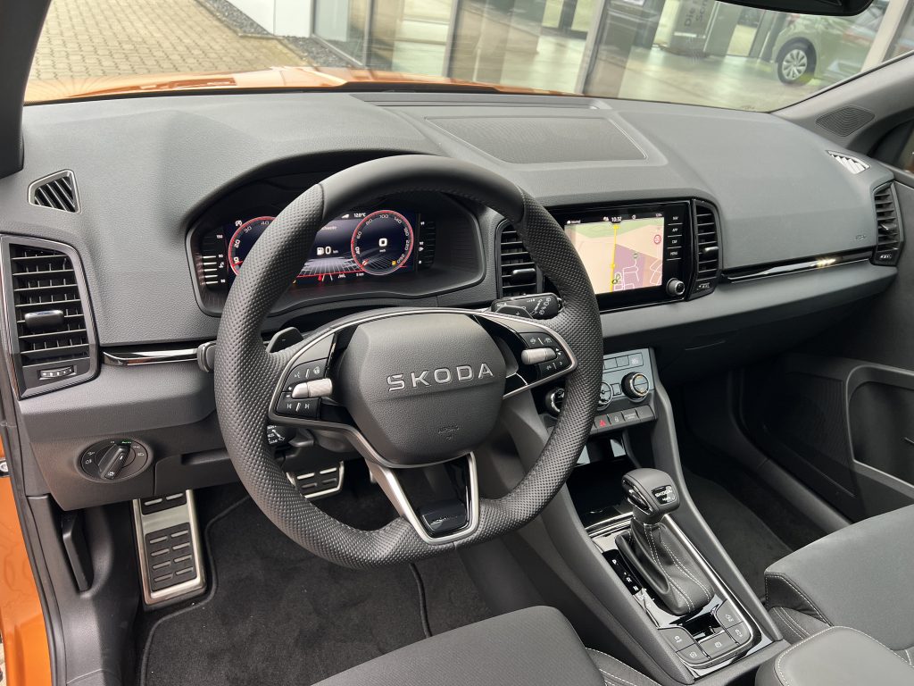 Driver’s view of a Skoda interior: digital gauges, steering wheel, center touchscreen showing a map, and gear shifter visible.
