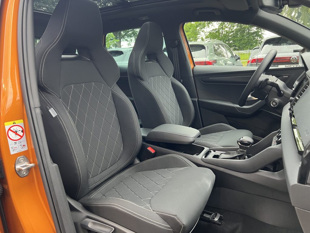 Right-hand drive car interior: black seats with white diamond stitching and orange door frame visible at the side.