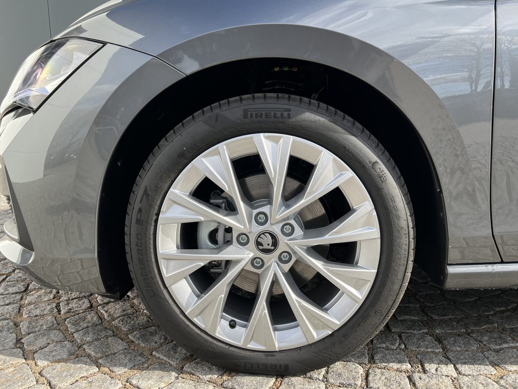Close-up of a gray car's front wheel, showing a silver alloy rim and a Pirelli tire under the fender.