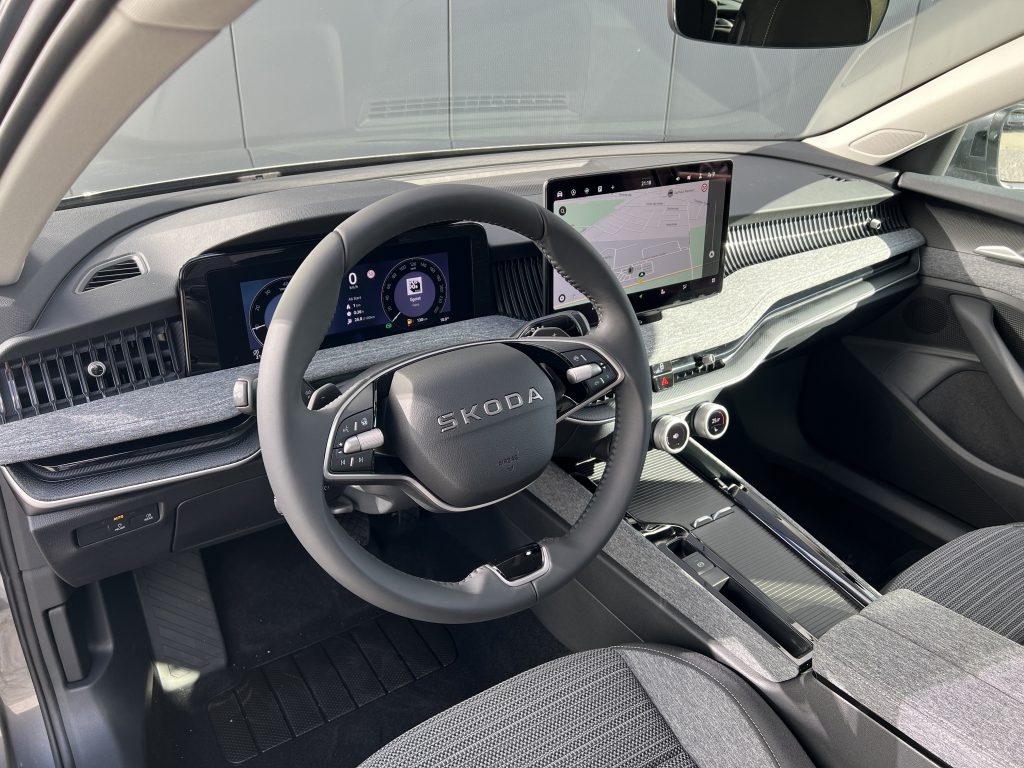 Inside a car cabin showing the steering wheel and a large central touchscreen displaying a navigation map.
