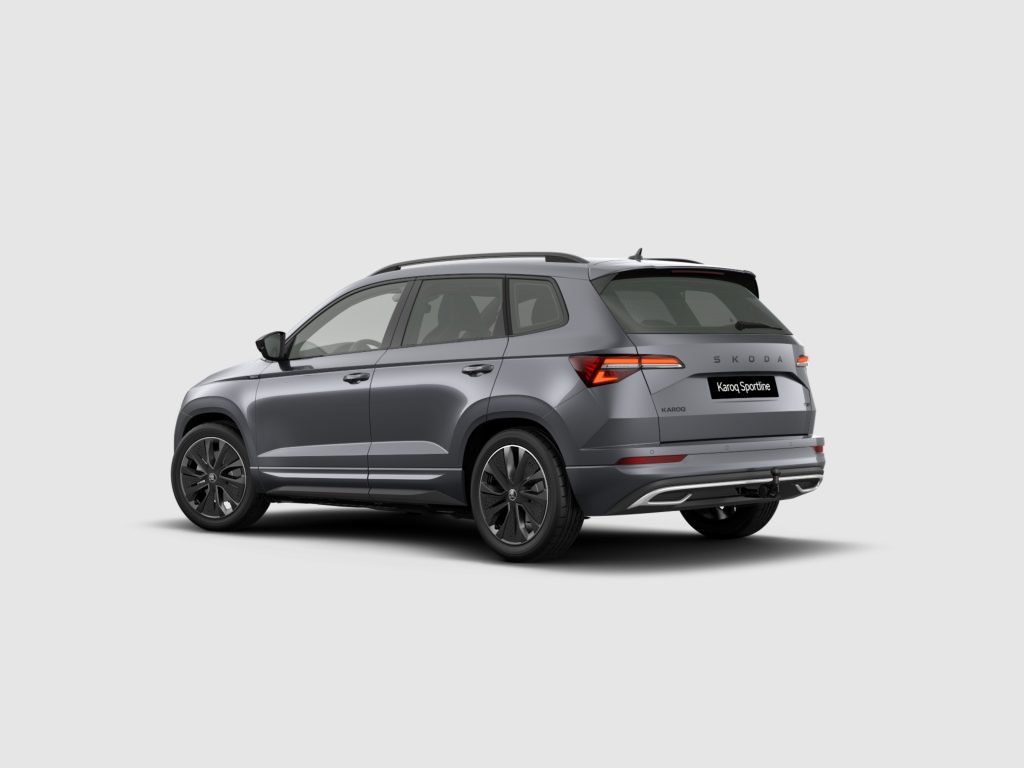 Rear-side view of a grey Skoda Karoq Sportline SUV, showing roof rails and taillights against a plain background.