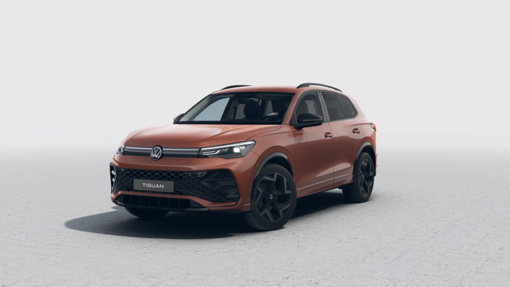 Orange Volkswagen Tiguan SUV photographed from the front-left with a light gray studio background, badge visible on the grille.”,