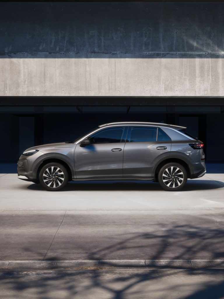 Silver SUV parked under a concrete building facade, side view with dark shadows above and sunlight on the lower wall and ground.
