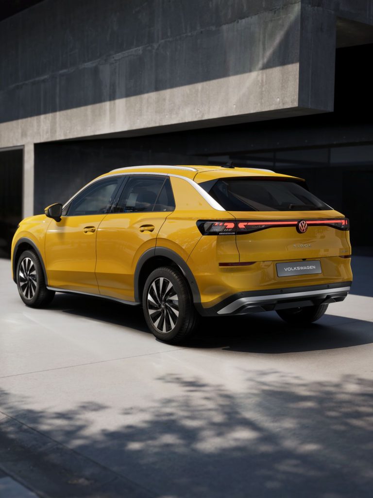 Yellow Volkswagen SUV (T-Roc) parked beside a concrete building, shown from rear-side angle.