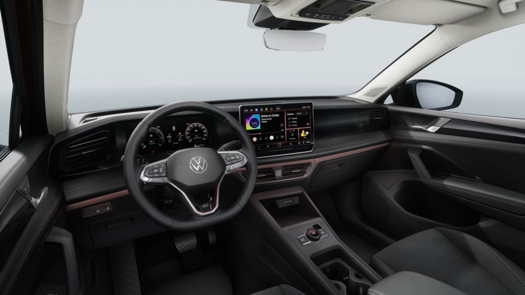 Interior of a modern car cockpit with steering wheel, digital gauges, and a large center touchscreen; sea visible through the windshield outside.