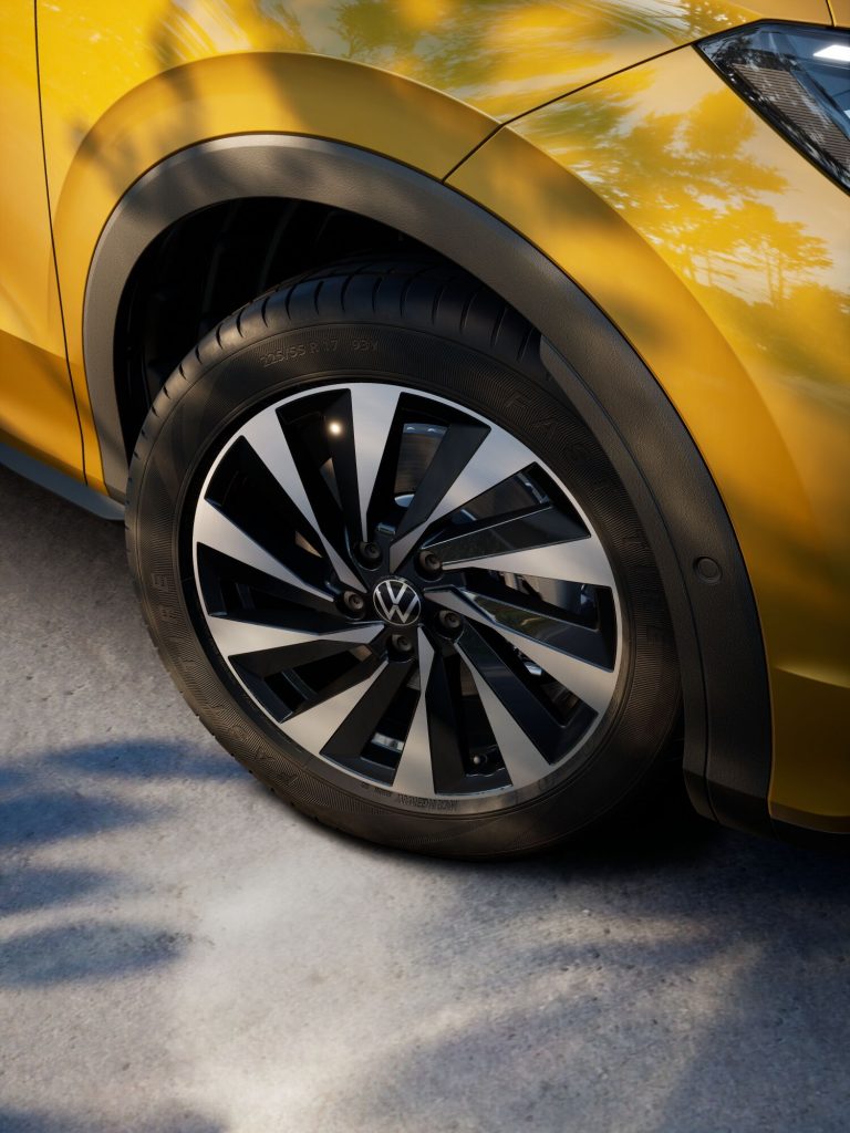 Close-up of a yellow car wheel and tire, showing a black and silver alloy rim with a VW emblem.