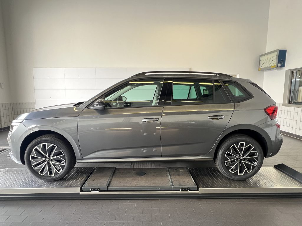 Gray SUV on an indoor vehicle lift in a bright showroom, visible wheels and roof rails.