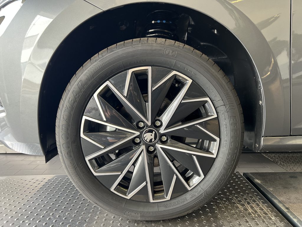 Close-up of a gray car wheel and tire, showing the black alloy rim and tread pattern mounted on the vehicle’s fender area