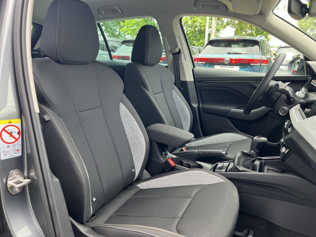 Interior of a car showing two front seats, steering wheel on the right, and dashboard with outside parked cars visible through the windows.