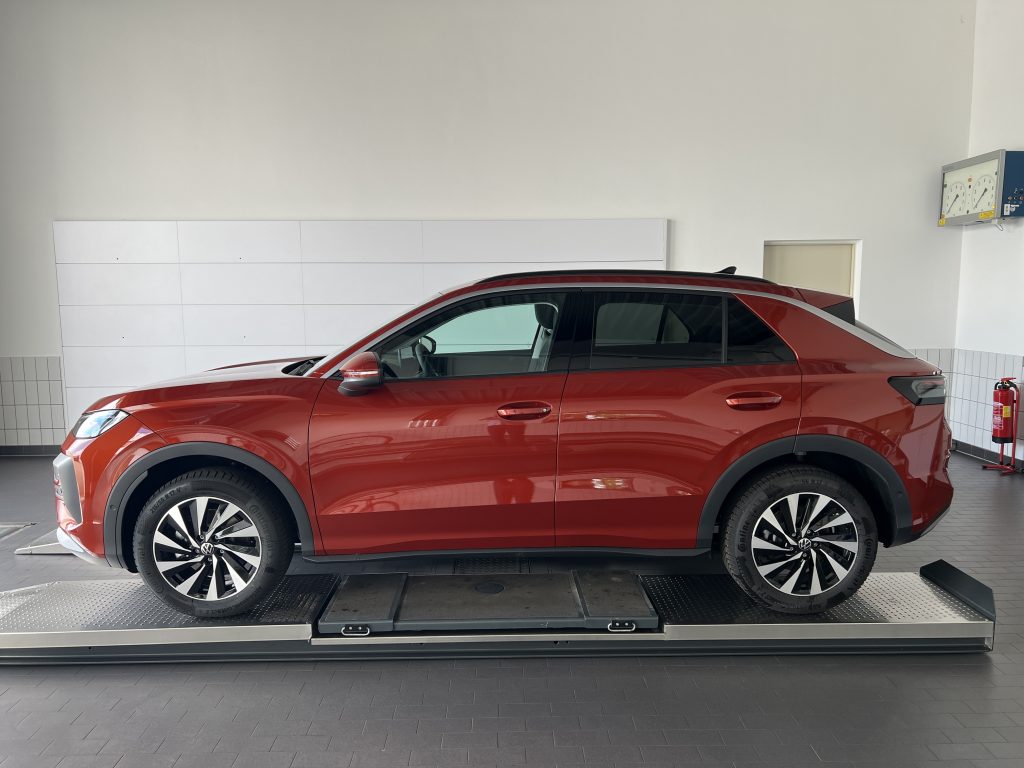 Red Volkswagen SUV on a metal service lift in a showroom with white tiled walls and a gray floor.