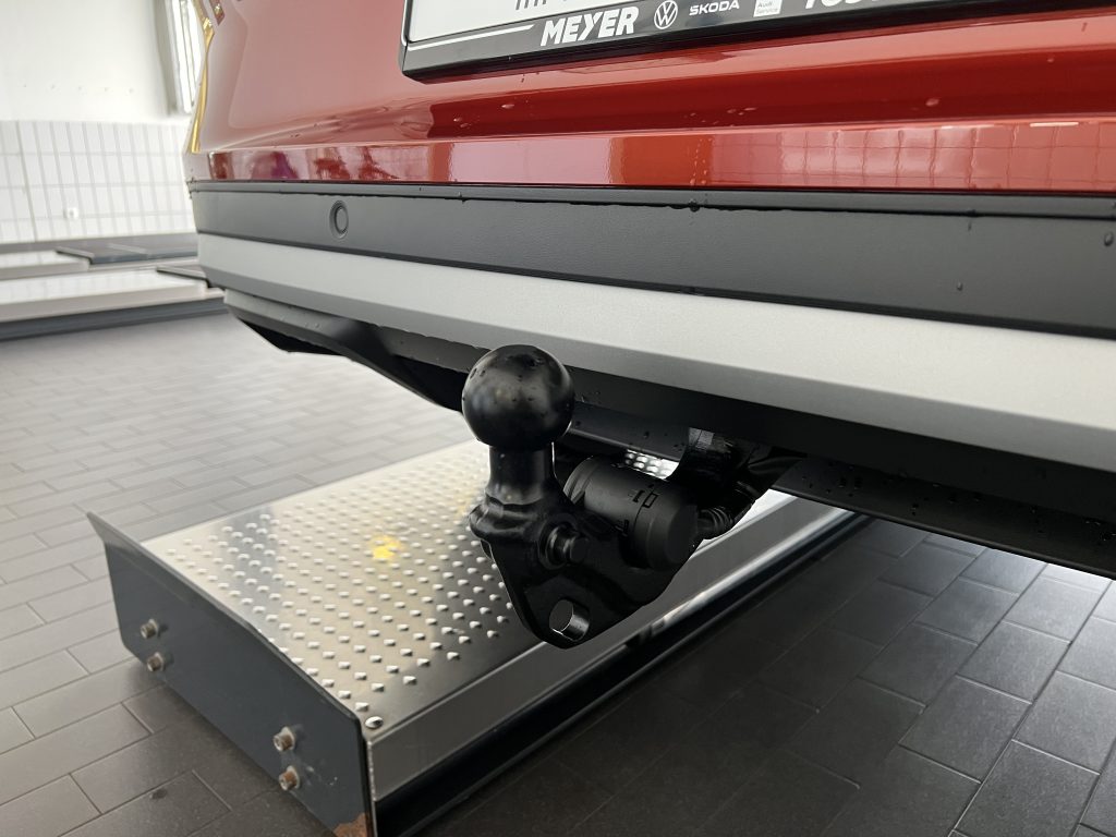Rear of a red car on a platform with a tow hitch ball and black bumper, diamond-plate step underneath.