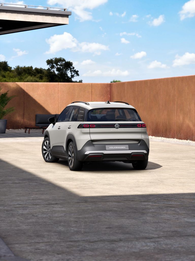 Rear view of a white Volkswagen ID. Cross SUV parked in a sunny courtyard with brown walls and a blue sky above.