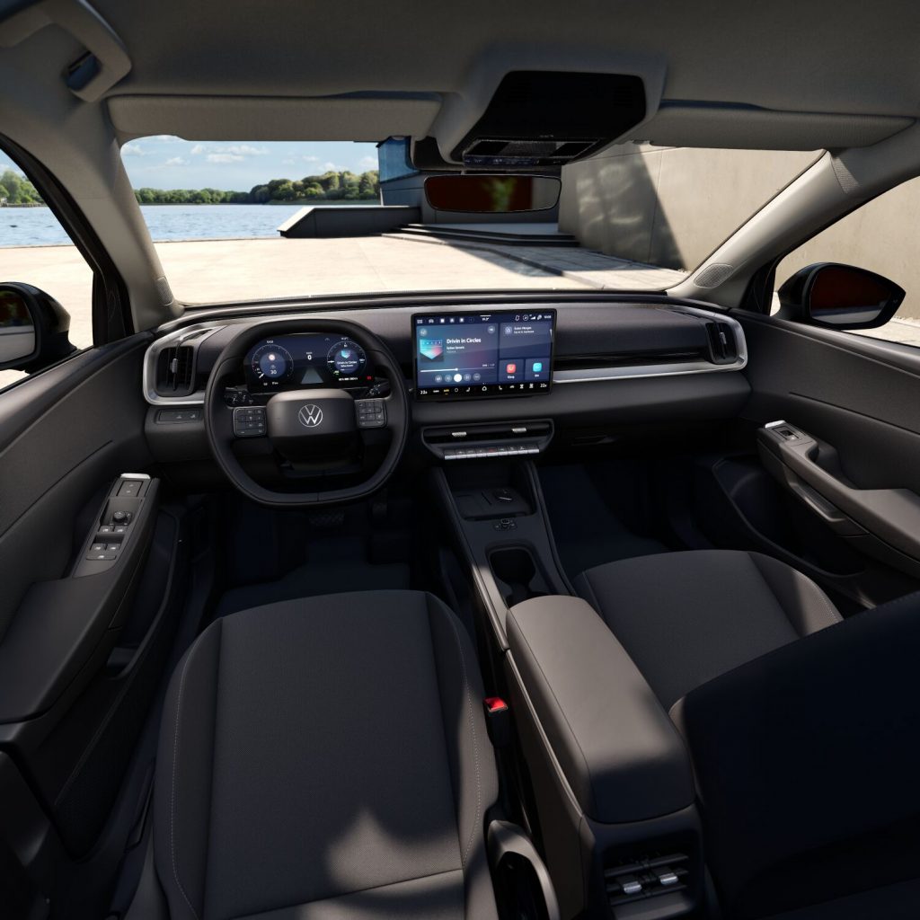 Modern car interior showing a digital instrument cluster and a large center touchscreen, view through windshield to water and quay outside