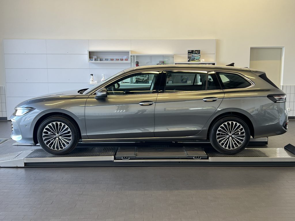 Side view of a silver SUV on a showroom hydraulic lift with white cabinetry in the background