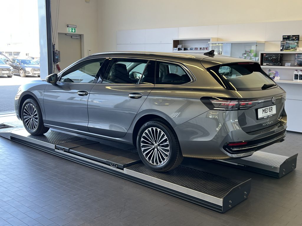 Grey SUV on a raised platform inside a car showroom, with shelves and product displays in the background.