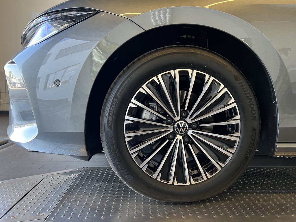 Close-up of the front left wheel and fender of a silver Volkswagen, showing a chrome multi-spoke alloy rim and Hankook tire in a showroom setting