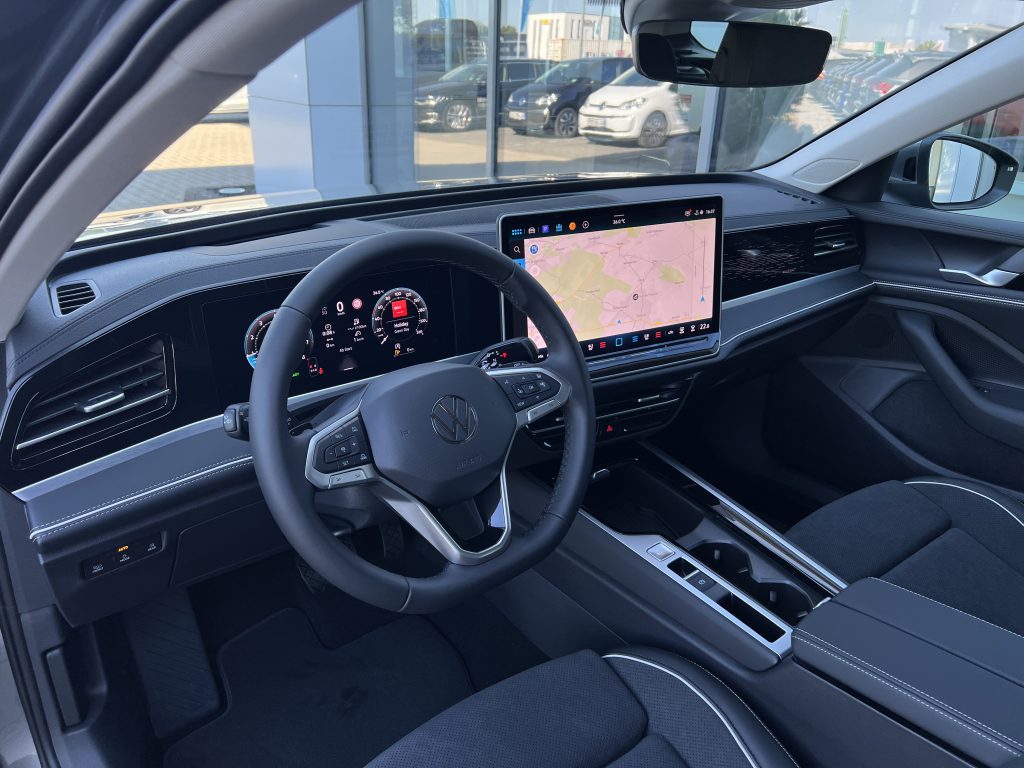 Modern car interior with a large central touchscreen map, steering wheel, and digital instrument cluster in a black-and-silver cabin, showroom visible through the windows.