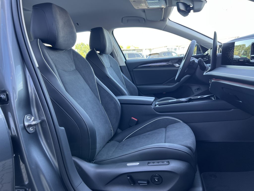 Front interior of a car with black seats, steering wheel, and a wide digital dashboard screen.